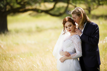 Young Bride and Groom couple in a summer garden. Tender holding each other. Redhead woman and blonde man with long hairs. Young family outdoor in nature. Love and tenderness