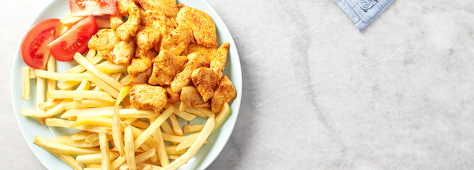 Fried chicken breast with tomatoes and french fries. Bright stone background. Top view. Copy space.