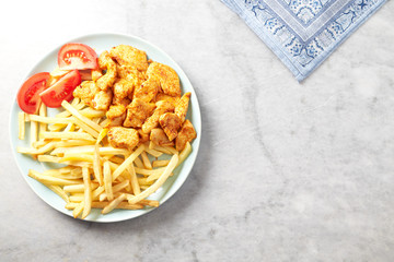 Fried chicken breast with tomatoes and french fries. Bright stone background. Top view. Copy space. 
