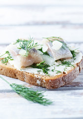 Tasty sandwich with cream cheese, salted herring and fresh herbs. Bright wooden background. Close up. 