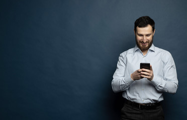 Happy bearded businessman using smartphone over blue background