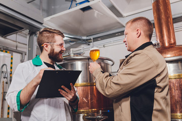 Mature man examining the quality of craft beer at brewery. Inspector working at alcohol manufacturing factory checking beer. Man in distillery checking quality control of draught beer.
