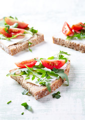 Tasty sandwiches with cream cheese, cherry tomatoes and fresh herbs. Bright wooden background. Close up. 