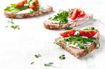Tasty sandwiches with cream cheese, cherry tomatoes and fresh herbs. Bright wooden background. Close up. 