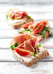 Tasty sandwiches with cream cheese, smoked ham and fresh herbs. Bright wooden background. 