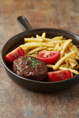 Fried hamburger steak with tomatoes and french fries. Rustic background. 