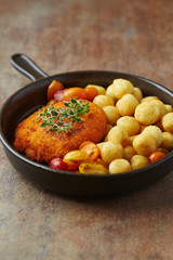 Breaded Chicken Breast with fried potatoes and fresh herbs. Rustic background.