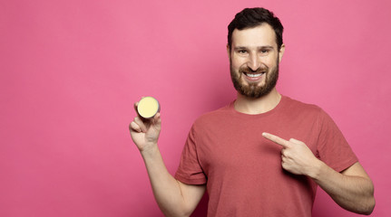 Close-up image of handsome bearded man holding beard balm on pink background.