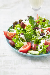 Healthy Salad with Tomatoes, Cucumber,  Lettuce and Olives on bright wooden Background. Healthy Snack Idea. 