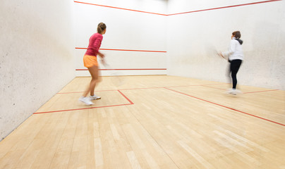 Fototapeta na wymiar Two female squash players in action on a squash court (motion blurred image; color toned image)
