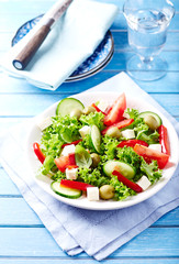 Healthy Salad with Tomatoes, Cucumber,  Lettuce, Olives and Feta Cheese on bright wooden Background. Healthy Snack Idea. 