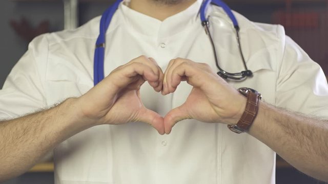 Close up of doctor with stethoscope showing heart gesture with his hands