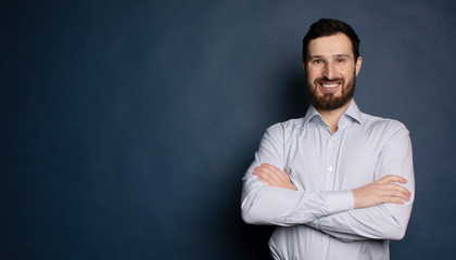 Happy bearded businessman looking at camera on blue background with copy space.