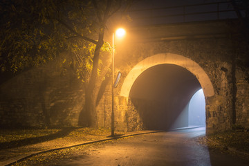 The Tunnel. Way out with spooky mist and fog at night. Single lamp and light from the other side. Afterlife concept.