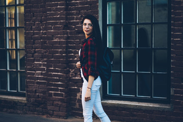 Attractive happy female person dressed in trendy clothes strolling at urban setting near to wall with advertising area for promotional.Pretty brunette woman having summer walk at string street
