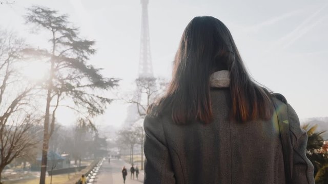 Camera follows happy elegant woman walking along autumn Paris towards famous Eiffel Tower on business trip slow motion.
