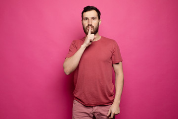 Fototapeta premium Bearded man placing finger on lips as if to say, shhhhh, be quiet, silence.