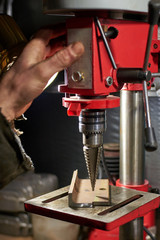Hands of a man who drills a metal part on a machine tool.
