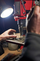 Hands of a man who drills a metal part on a machine tool.