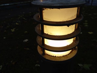Street lamp in a city park. Frosted glass with frosted warm yellow light. A metal rim or cage in...
