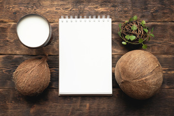 Coconut milk in cup and coconut and blank page notepad with copy space on brown wooden table background.