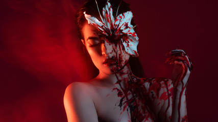 Blood Lily, scary and sexy Halloween look. Beautiful young brunette girl on red background.