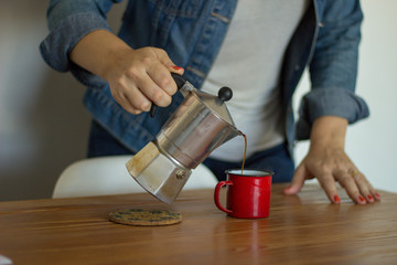 woman serving coffee from italian coffee maker on a wooden table at home