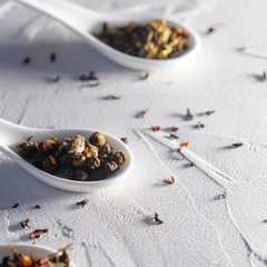 Fototapeta na wymiar Different varieties of tea leaves in white measuring spoons on a white textured background. To brew tea