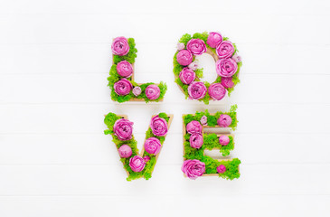 Volume letters LOVE with stabilized moss and roses on white wooden background with copy space