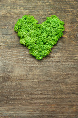 Green stabilized moss in a heart shape on wooden background