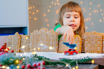 Girl playing with car toy with Christmas tree in gingerbread cookies town