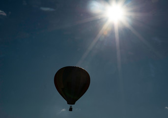 Silhouette of hot air balloon flying beneath the sun.