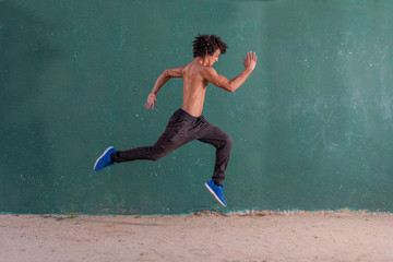 Handsome and fit young man no shirt running on the ground and frozen in the air. Free running parkour.