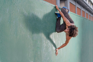 Handsome young man no shirt climbing a wall and suspended just like a real spiderman. Free running parkour © Omar Bahena