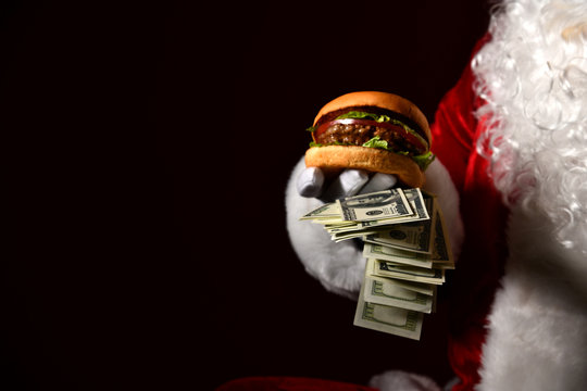Santa Claus hold bunch of dollars money in one hand and big double beef burger sandwich. Fast food concept
