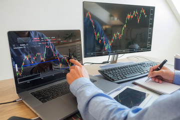 Trading on the table is working on a computer screen full of charts and data analysis and stock...