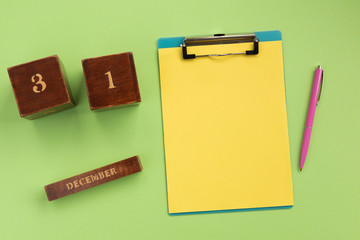 Christmas or New Year planning concept. Clipboard, wooden calendar,  pen, on green background. Flat lay, top view, copy space.