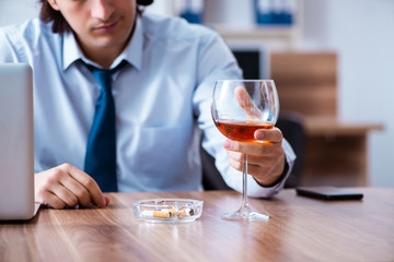 Male employee drinking alcohol and smoking cigarettes at workpla