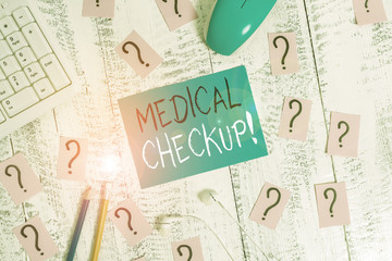 Text sign showing Medical Checkup. Business photo text thorough physical examination includes variety of tests Writing tools, computer stuff and scribbled paper on top of wooden table