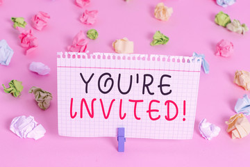 Writing note showing You Re Invited. Business concept for make a polite friendly request to someone go somewhere Colored crumpled papers empty reminder pink floor background clothespin