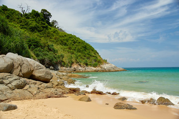 A beach with large stones, the sea and green hills.