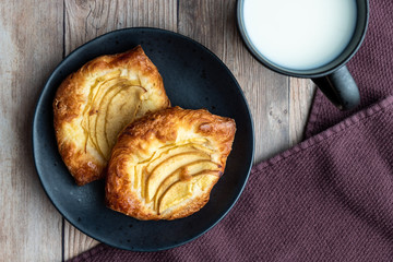 Fresh individual apple tarts on a black plate, cup of milk, purple cloth napkin, wood background