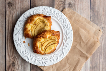 Fresh individual apple tarts on a white plate, brown paper sacks, wood background