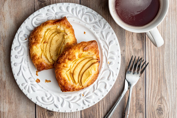 Fresh individual apple tarts on a white plate, forks, cup of hot tea, wood background