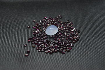 Natural Chalcedony in a shape of cobochon on a natural rhodolite garnet and on a black fabric background.