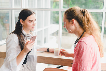 Two beautiful young women drinking coffee and playing phone. concept of relaxation.