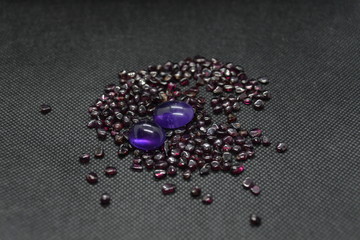 Natural Amethyst in a shape of cobochon on a natural rhodolite garnet and on a black fabric background.
