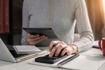 Female businessman hand using calculator and writing make note with calculate about cost at home office. 