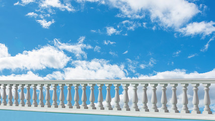 White railing of a summer veranda against a clear sky with clouds on a sunny day