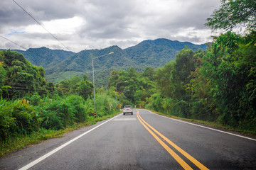 Blurred background of a mountain road view, from a car windscreen that runs with care, with natural scenery surrounded by plants, large trees